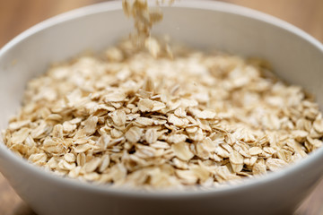 oat flakes fall in white bowl on wood table