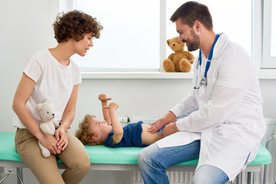 Portrait of smiling doctor examining stomach of little boy and asking him to say where it hurts