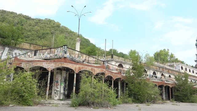 Tourist walking on abandoned building, murals and minaret in Consonno, Italy. Rusted construction with graffiti and wild vegetation, desolate and scary place, ghost town