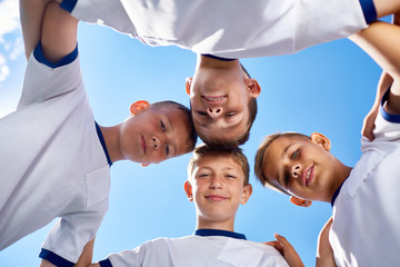 Fototapeta na wymiar Low angle portrait of junior football team standing in circle and smiling at camera against blue sky
