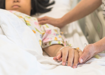 Fototapeta na wymiar Nursing caretaker concept with kid patient sleeping in bed with family caregiver hand support in blur medical hospital background (focus on hand)