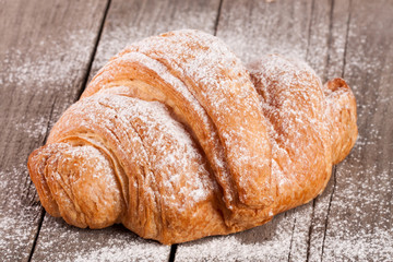 croissant sprinkled with powdered sugar on old wooden board