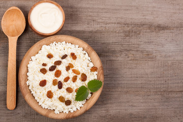 Cottage cheese in bowl with sour cream and raisins on old wooden background with copy space for your text. Top view