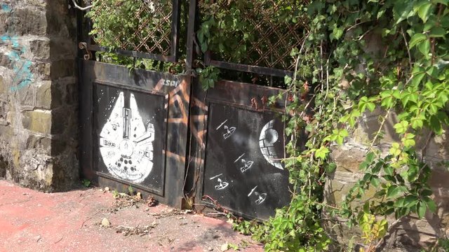 Abandoned iron gate with spaceship graffiti and wild vegetation, Consonno, Italy