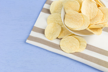 crispy potato chips on cotton fabric with light blue wooden background