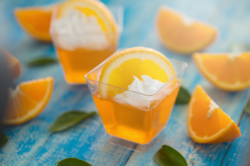 Orange jelly in a cup with whipped cream and orange sliced on blue wooden  background