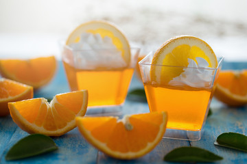 Orange jelly in a cup with whipped cream and orange sliced on blue wooden  background