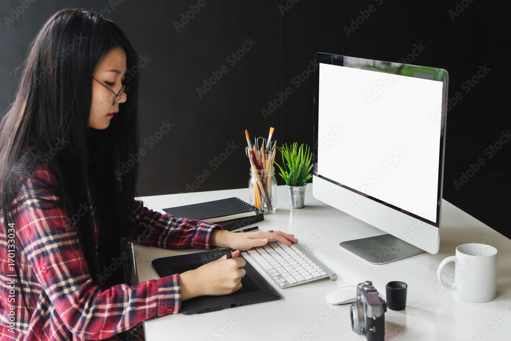 Poster female graphic designer working on computer while using graphic tablet at desk in the office