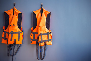 orange life jackets hanged on plain grey wall by swimming pool for emergency, filter effect