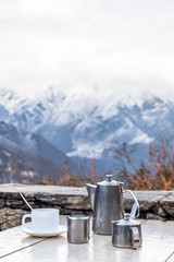A kettle with coffee, milk jug and a cup with a view to Himalaya mountains and Everest in clouds. The best coffee time in the world, Everest View Point, Khumjung, Sagarmatha National Park, Nepal. 