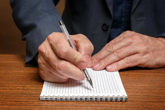 A man is making notes in a notebook sitting at a wooden table