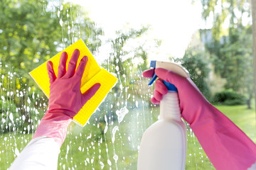 Female hands in pink gloves cleaning window with yellow rag and spray detergent. Spring cleanup,...