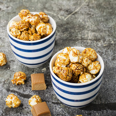 Sweet caramel popcorn in two ceramic white striped blue bowls on a stylish gray stone background. Selective focus.