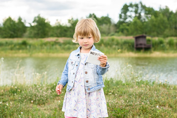 Sad lovely little baby girl with a spinner toy in the hands walks around a small lake outdoors in...