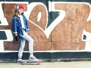 Cute girl in a baseball cap with a skateboard on a dark background.Sport.