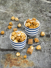 Sweet caramel popcorn in two ceramic white striped blue bowls on a stylish gray stone background. Selective focus.