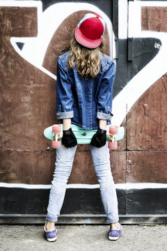 Cute girl in a baseball cap with a skateboard on a dark background.Sport.