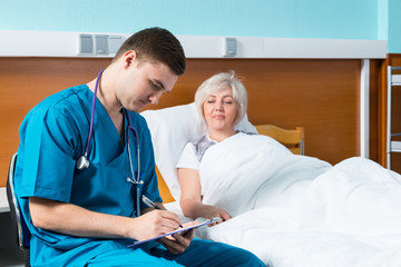 Handsome male doctor in uniform with phonendoscope on his neck writing down complaints of patient