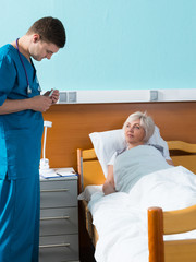 Young handsome male doctor in uniform with phonendoscope on his neck looking at a thermometer of his patient