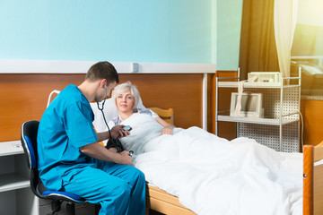 Doctor in uniform with phonendoscope on his neck is measuring the arterial pressure of his female patient