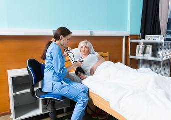 Obraz premium Young female doctor in uniform with phonendoscope is measuring the arterial pressure of her patient using a medical equipment
