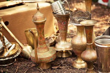 Fototapeta na wymiar Antique Indian handicraft etched vases and surahi jug at a flea market. Old brass tableware collectibles at a garage sale