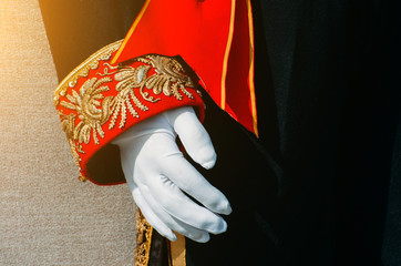 Black men's historical clothing with red and gold patterned insets on the sleeve, a hand in white...