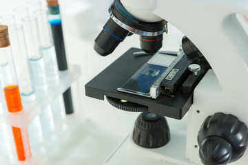 Modern microscope on the workplace near test tubes with liquid