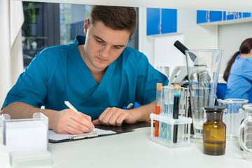 Young male scientist in uniform writing down notes of his research in a laboratory