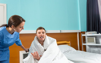 Fototapeta premium Beautiful nurse giving pills to ill patient sitting on wheelchair covered with quilt in hospital ward