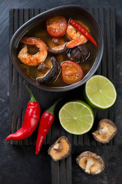 Bowl of spicy Tom Yum Thai soup on a black wooden serving board, above view, studio shot