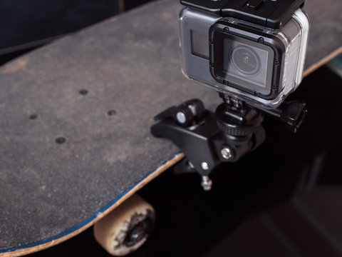 Action camera for professional video shooting of extreme sport tricks, training and competitions, fixed on skateboard rubbed deck on black background