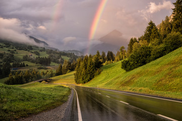 Regenbogen über einer Straße in der Schweiz beim Sonnenuntergang