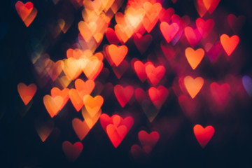 Abstract background of colorful hearts on black backdrop. Bokeh of defocused glitters, blurred pink and orange symbols of love. Festive wallpaper of holidays and celebrations, St. Valentine's day
