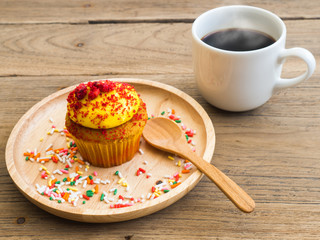 Yellow cupcakes put on a spherical wooden plate. Beside of cupcake have white coffee mug.All of it rests on wooden table.
