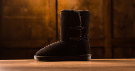 One winter boot on wooden desk. Cozy black shoes for cold winter.