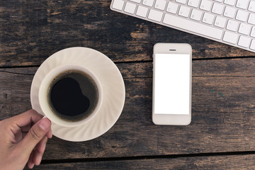 Close up of women's hands holding smart phone with  blank screen with hot coffee cup on wooden table top view.