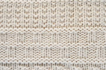 The texture of a knitted sweater is a thick beige string. Part of a sweater with various kinds of patterns close-up