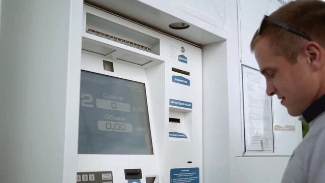 The guy puts the money in the bill acceptor. The young man pays for gasoline.