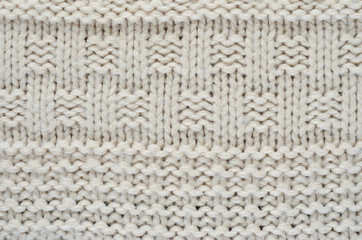 The texture of a knitted sweater is a thick beige string. Part of a sweater with various kinds of patterns close-up