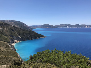 The coast of Kefalonia in Greece with its turquoise sea, blue sky and green mountains.