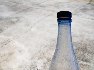 Top part clear transparent bottle with evaporated water dew attached pattern, blue cap, blurred dirty cement floor background