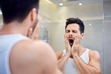 Sleepy young man standing in bathroom yawning