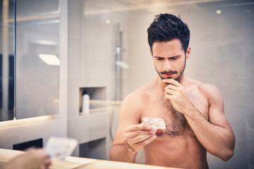 Focused handsome young man reading from medicine package in the bathroom