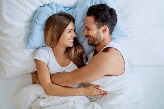 Happy young couple embracing and looking at each other while lying in bed together