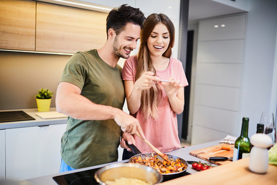 Cute young couple cooking together in kitchen and taking photo of their food