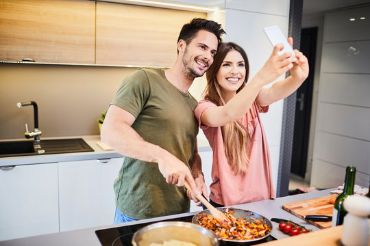 Loving young couple in the kitchen cooking together and takng selfie laughing