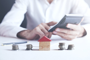 Businessman Calculating Tax In Front Of Stacked Coins And House Models