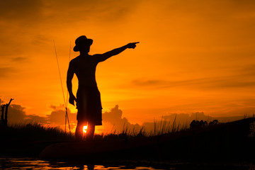 Silhouette of fisherman on the boat pointing with finger in sky.
