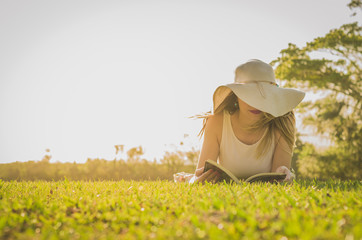 Linda mulher lendo um livro no gramado verde, sol de verão.